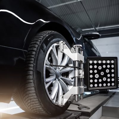 CLose-up car wheel indoors service maintenance repair center against laser sensor equipment diagnostics and 3d wheel alignment. Vehicle inside garage workshop for auto camber toe check fixing work.