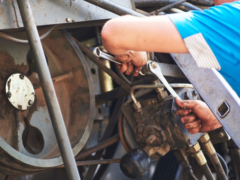 Combine machine service, mechanic repairing motor outdoors.