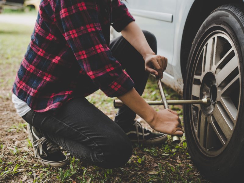 Young hipster woman checking out a flat tyre on her car try to fix.